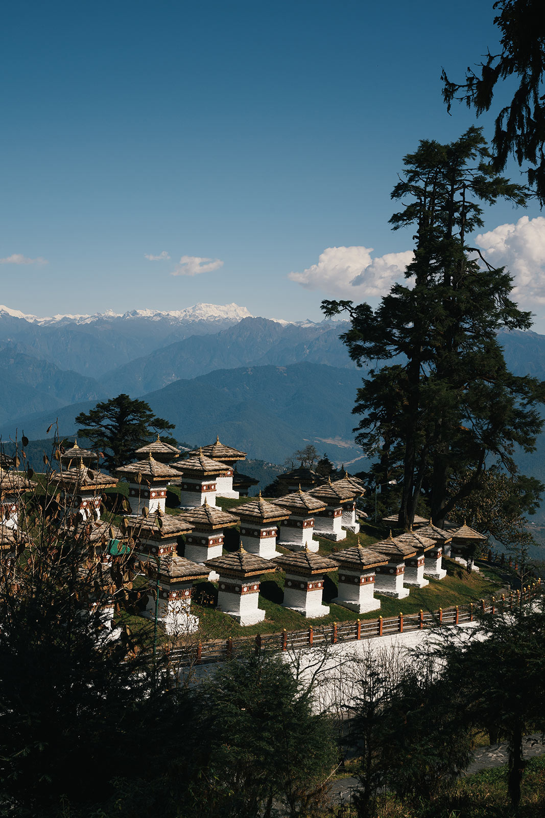 Dochula Pass: A scenic mountain pass in Bhutan, featuring the 108 Druk Wangyal Chortens (stupas) arranged in a picturesque array on a grassy ridge. The pass offers panoramic views of the snow-capped Himalayan peaks, with lush green hills and misty clouds adding to the serene and spiritual atmosphere of the site.